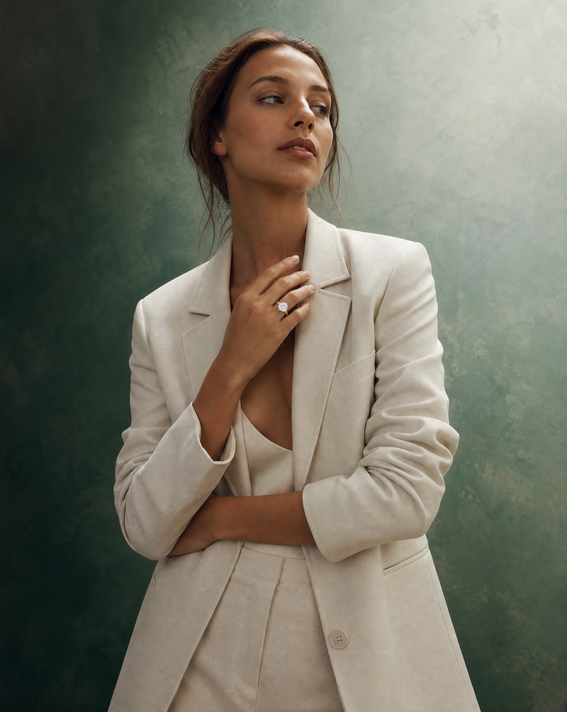 Woman in a cream suit wearing a solitaire diamond engagement ring against a green backdrop