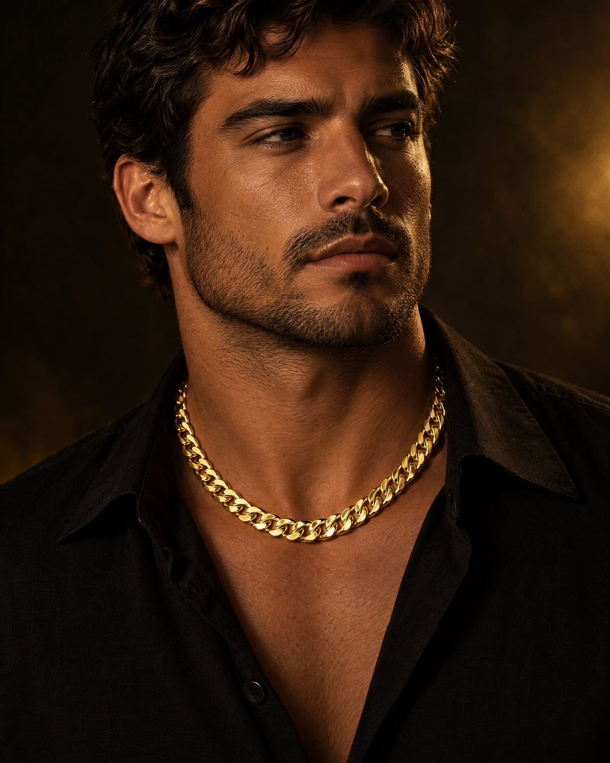 Man wearing a 14K yellow gold Miami Cuban link chain over an open black shirt in warm, low light