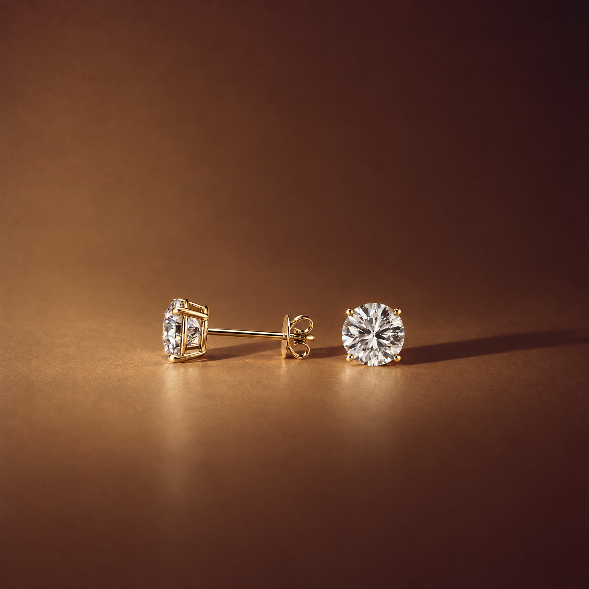 Pair of 1 carat round lab-grown diamond stud earrings in 14K yellow gold, one shown side-on with its four-prong basket, post and push back, brown background, AI-generated image — DEEVE