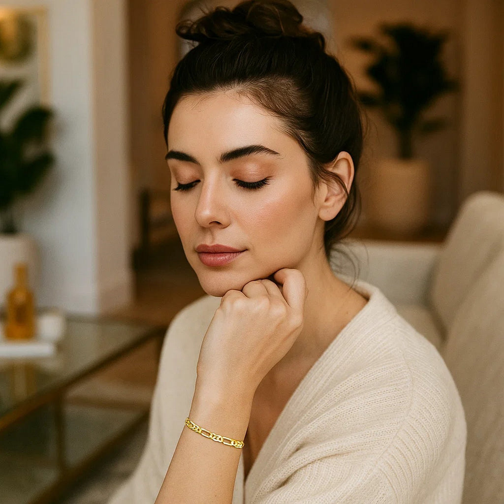 Gold bracelet worn by a woman in a cream sweater, chin resting on her hand
