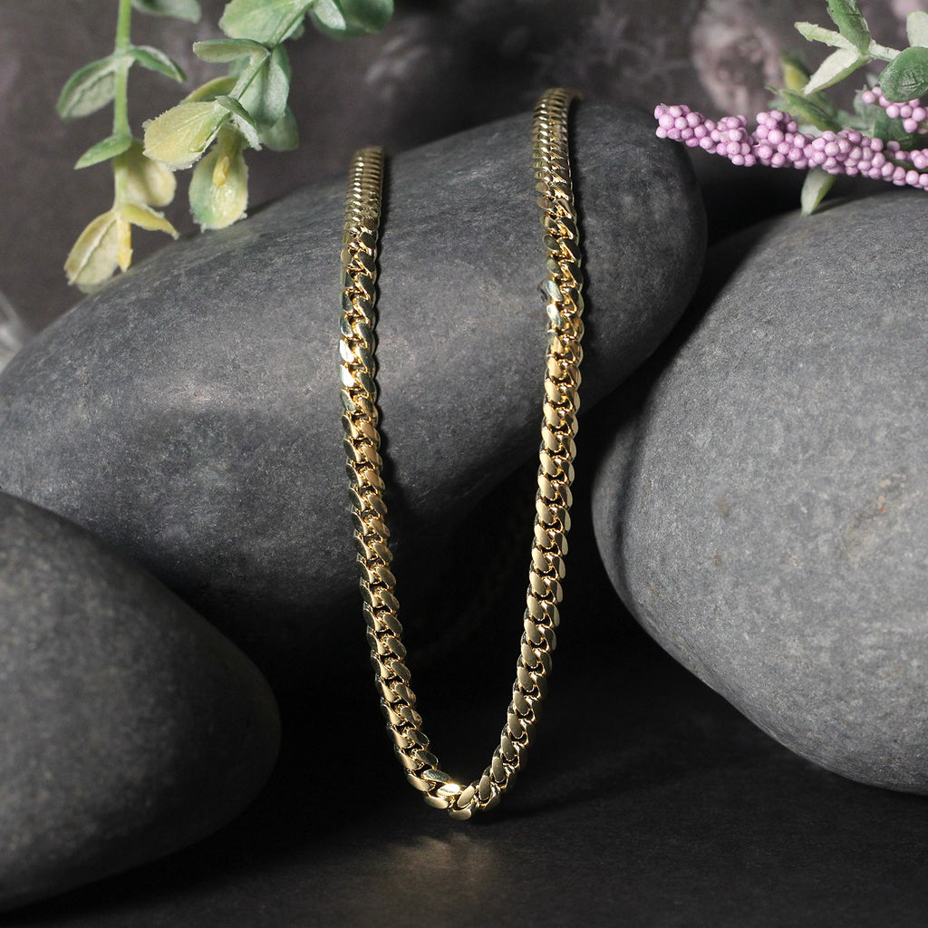 Solid Miami Cuban chain in 14K yellow gold draped over two stones