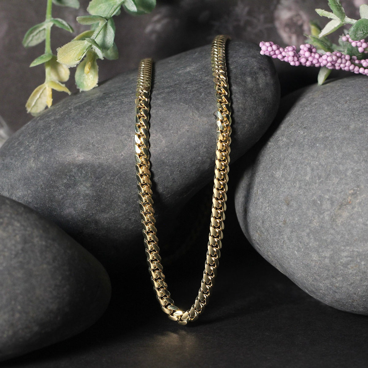 Solid Miami Cuban chain in 14K yellow gold draped over two stones