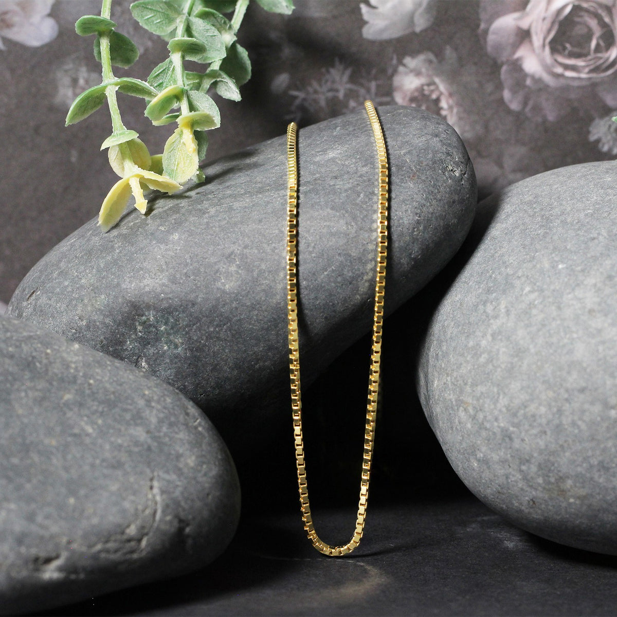 Box chain in 14K yellow gold draped over two stones