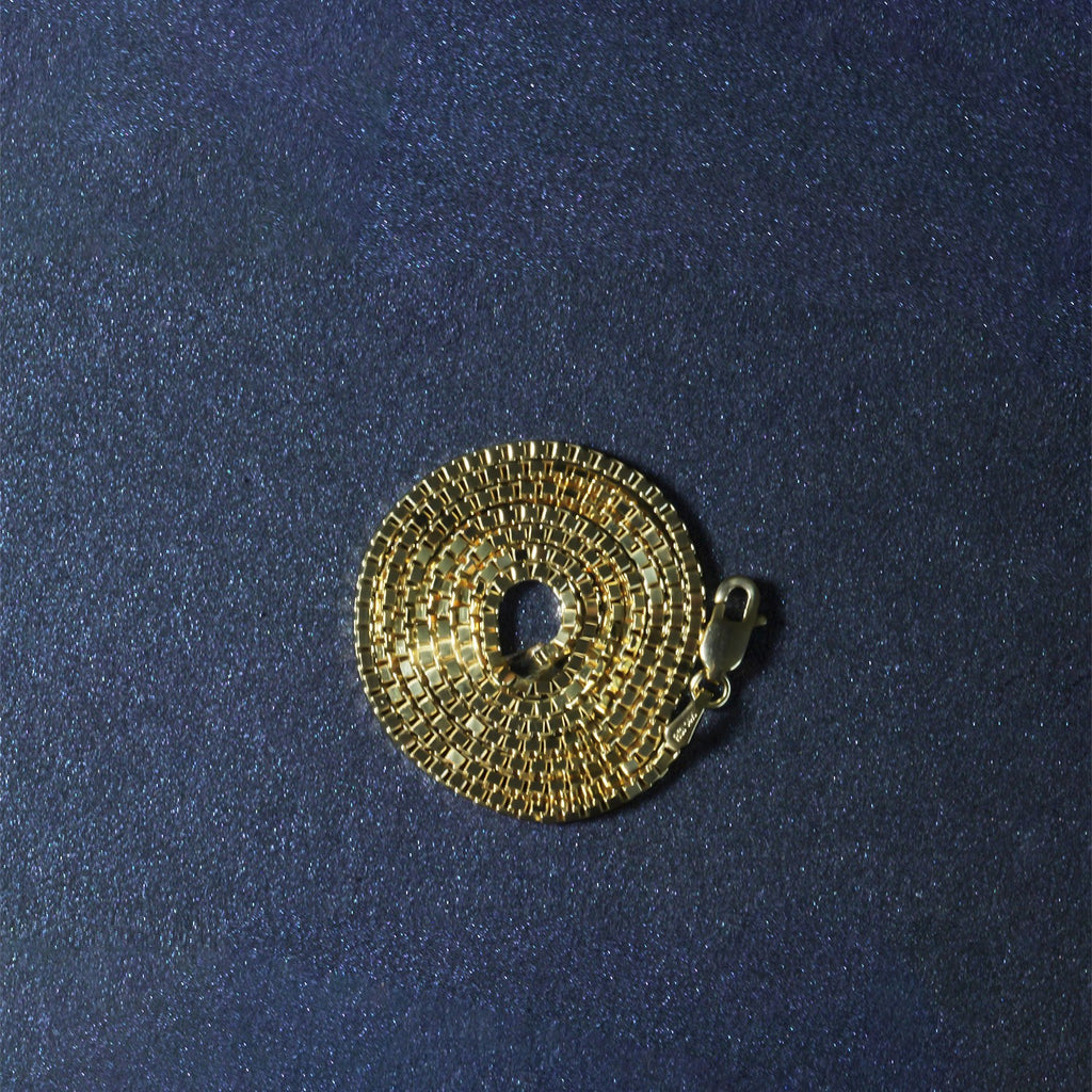 14K yellow gold box chain, 1.4mm, coiled on a dark surface