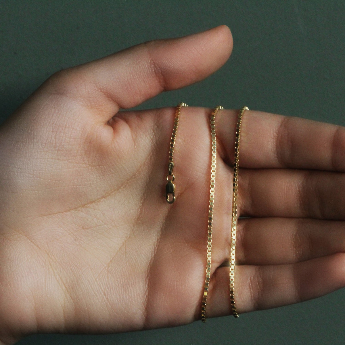 1.4mm box chain in 14K yellow gold held across an open palm