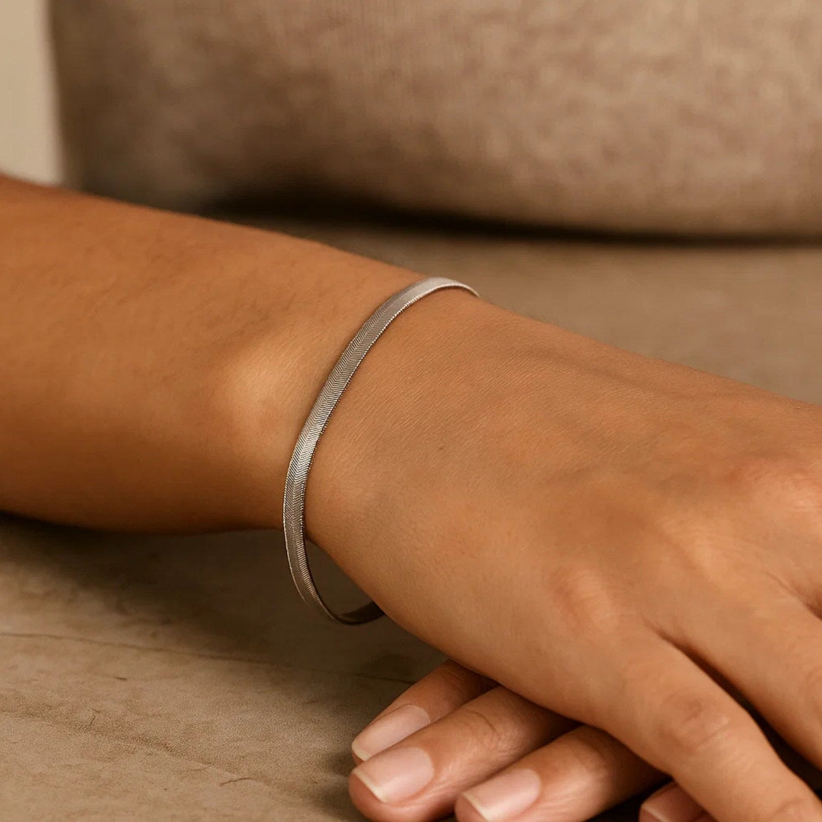 Herringbone bracelet in 14K white gold worn, wrist resting on a table