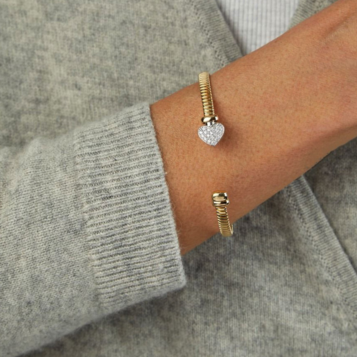 14K two-tone diamond heart cuff worn on the wrist with a grey sweater
