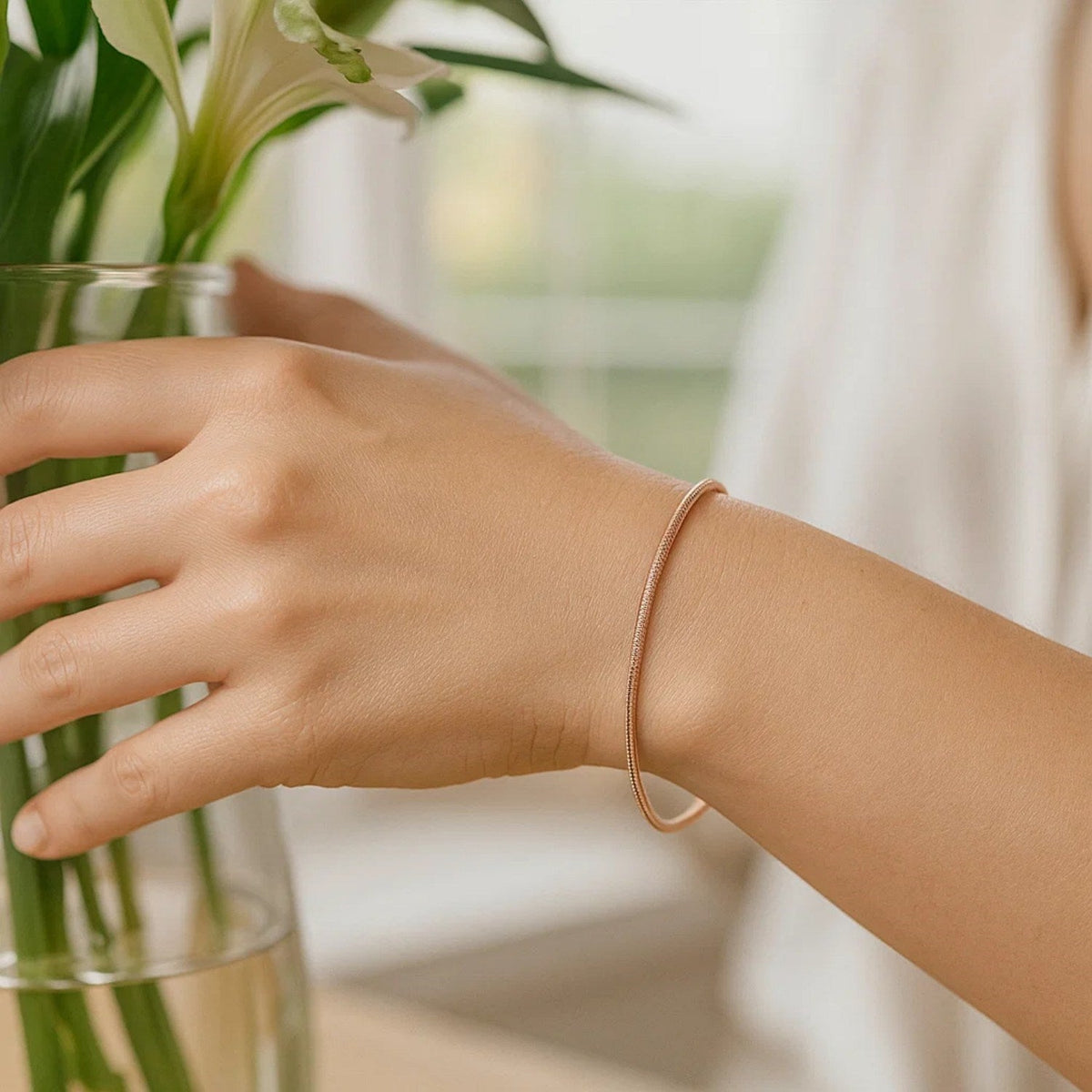 14K rose gold diamond-cut stack bangle worn on the wrist beside a vase