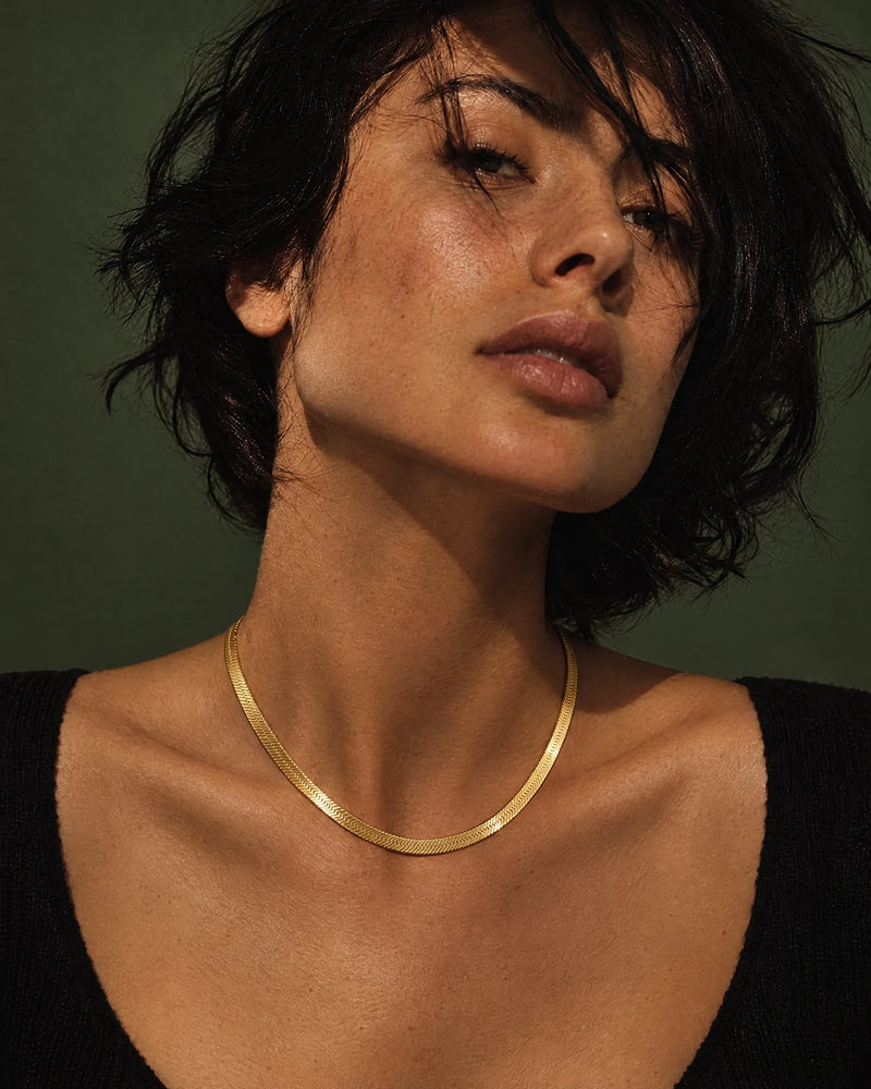 Gold chains: 6 mm herringbone chain in 14K yellow gold worn at the collarbone — AI-generated image — DEEVE