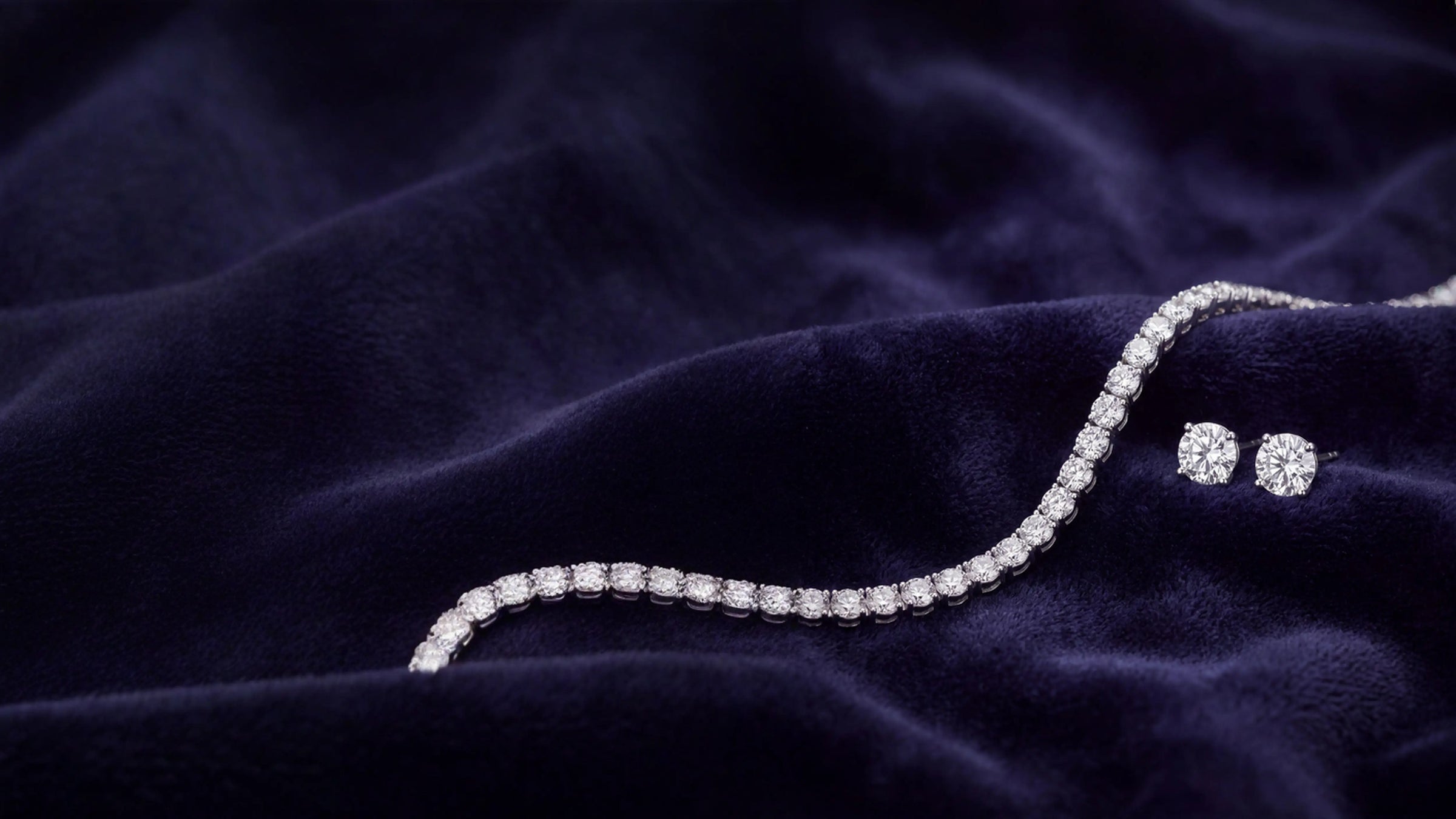 A diamond tennis bracelet and matching stud earrings displayed on a dark navy velvet fabric background. DEEVE Canada